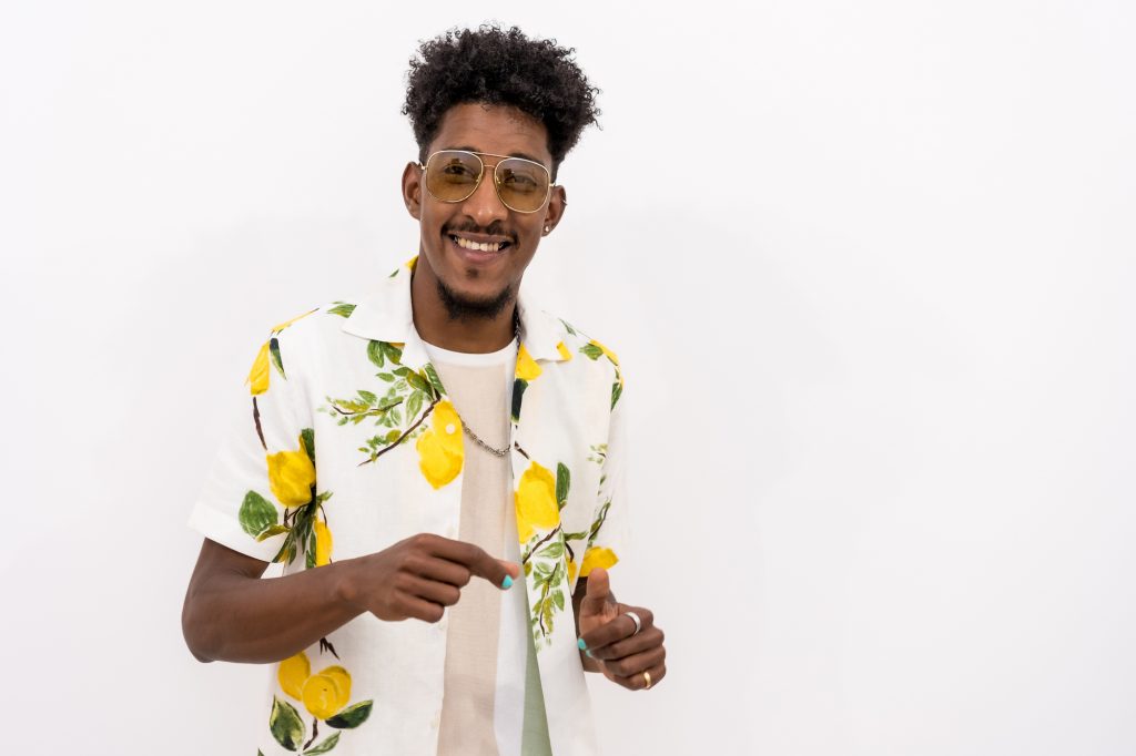 A Young Cuban Man With A Floral Shirt And Glasses Smiling On A White Background, Copy And Paste Space