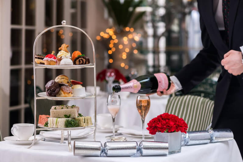 Table set with a variety of desserts, glasses of champagne, and silver afternoon tea crackers.