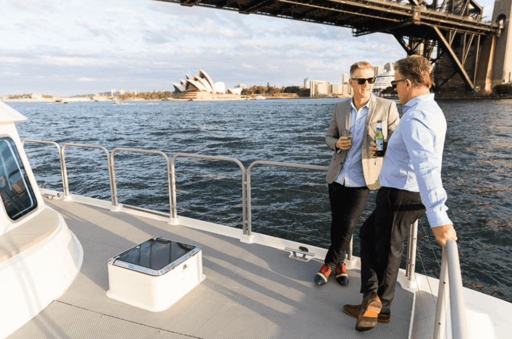 two elegantly dressed men on a boat trip overwieving the Sydney Opera House