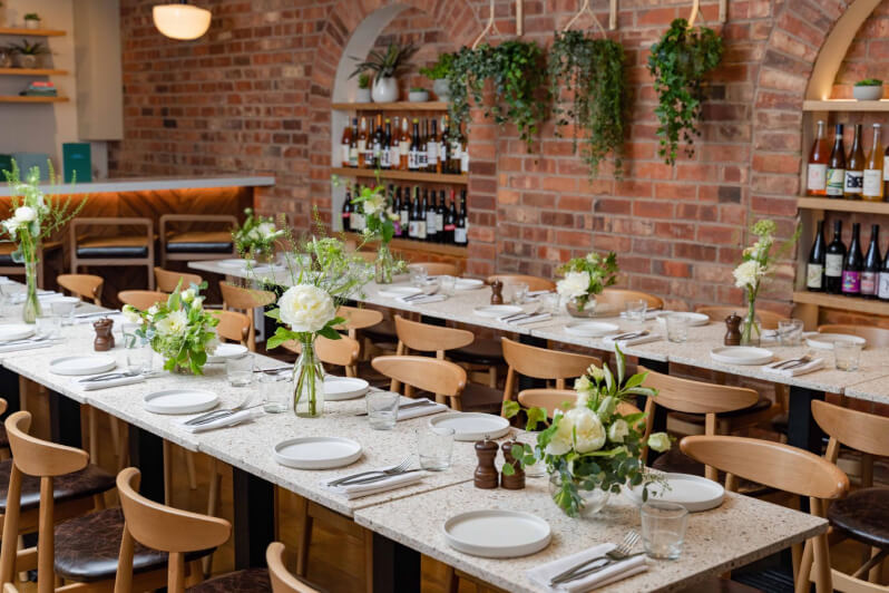 Modern venue with brick walls. wooden furniture, and a lot of plants.