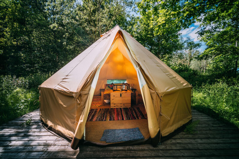 Glamping tent with a bed inside, surrounded by trees.