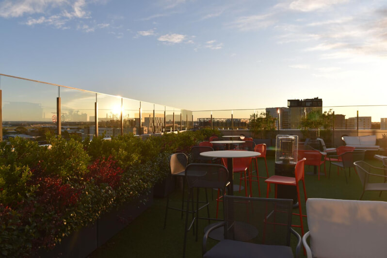 Rooftop terrace lined with plants, overlooking a panorama of the city.