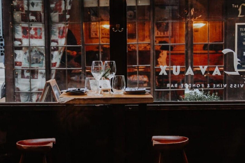 Look out of the window of a cosy restaurant; It has wooden details and an intimate table set with wine glasses.