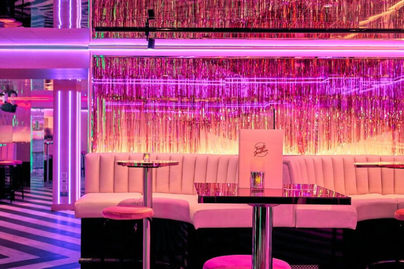 Pink venue with neon lights, white lounges, and sparkly decor.