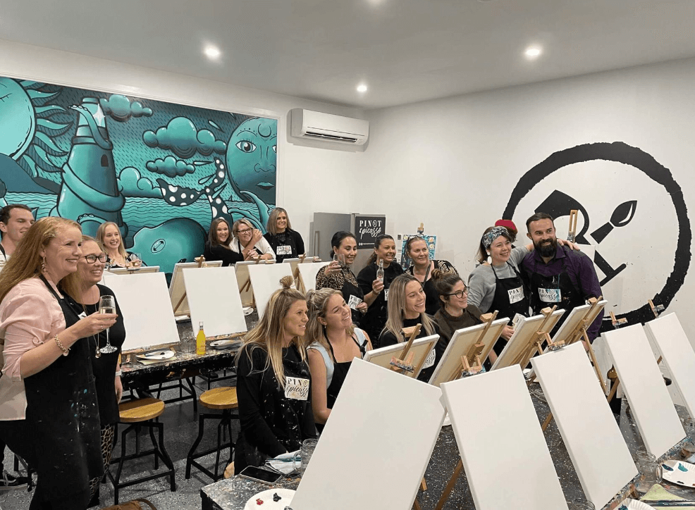 a group of smiling people holding glasses in front of canvas