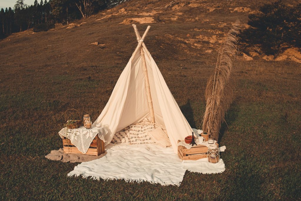 A teepee set up outdoors, featuring a blanket, pillows, and boho-style decorative items.