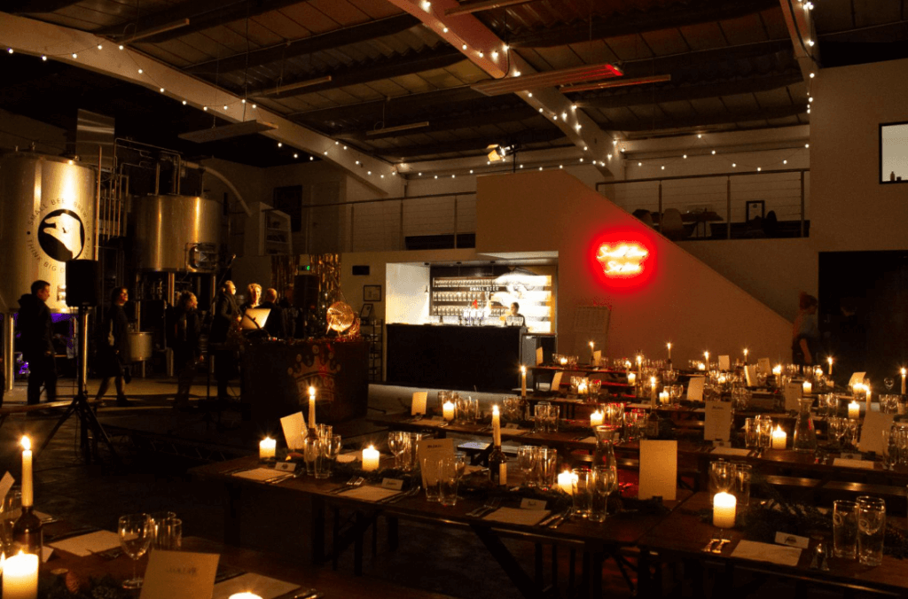 Inside of a brewery with tables set up for guests, decorated with fairy lights