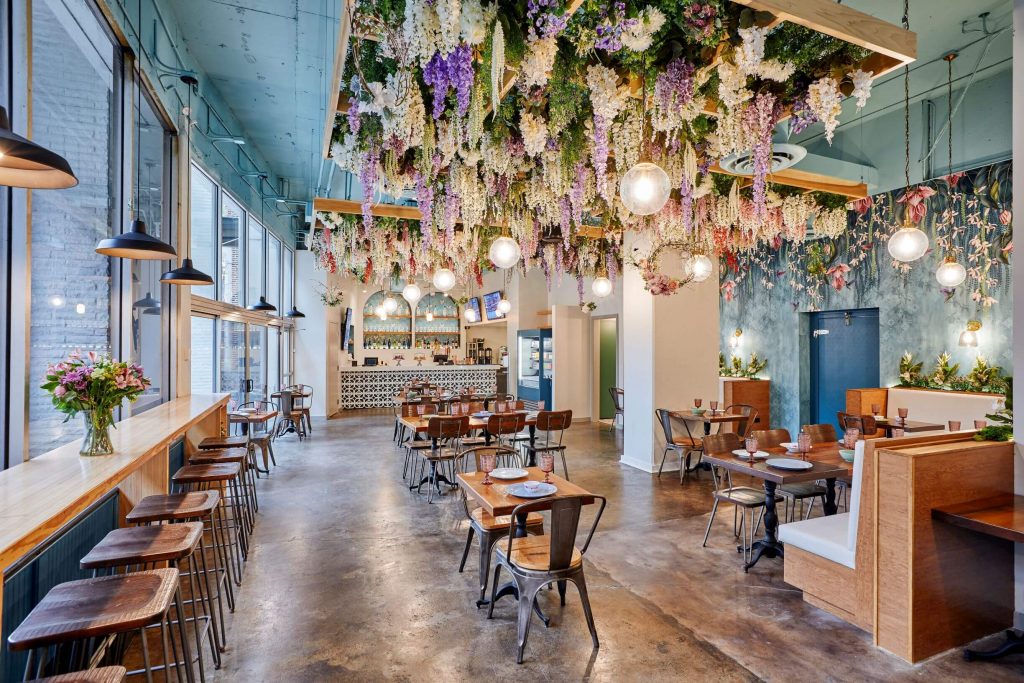 An elegant restaurant interior with a floral pattern on the wall and flower decorations hung from the ceiling.