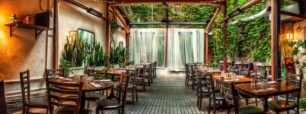 An outdoor garden room with green foliage at a New York restaurant.
