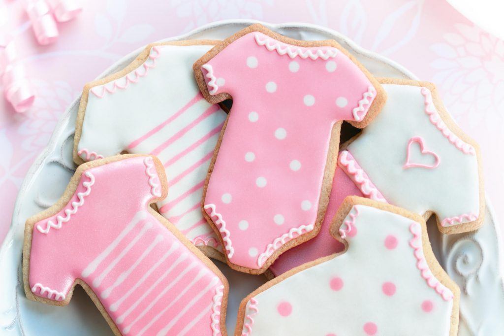 A tray of pink and white cookies shaped like baby onesies.