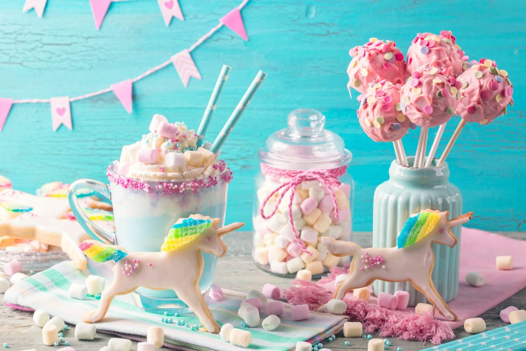 A candy display featuring pink lollipops, colourful marshmallows, and unicorn-shaped cookies with rainbow manes.
