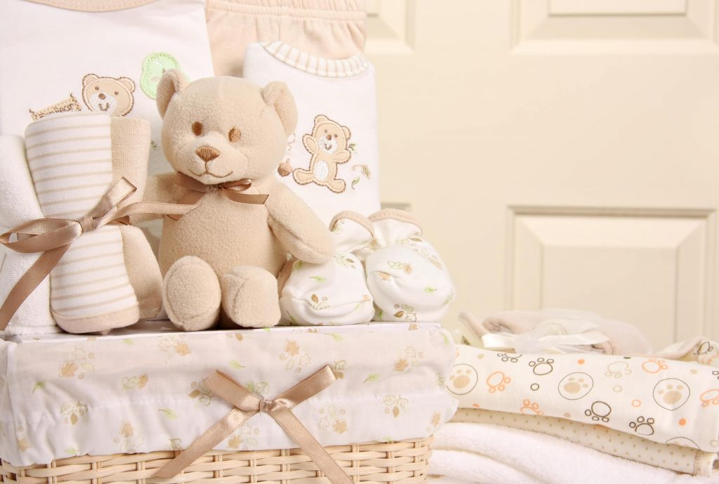 A gift basket with a teddy bear, blankets, and baby clothes.