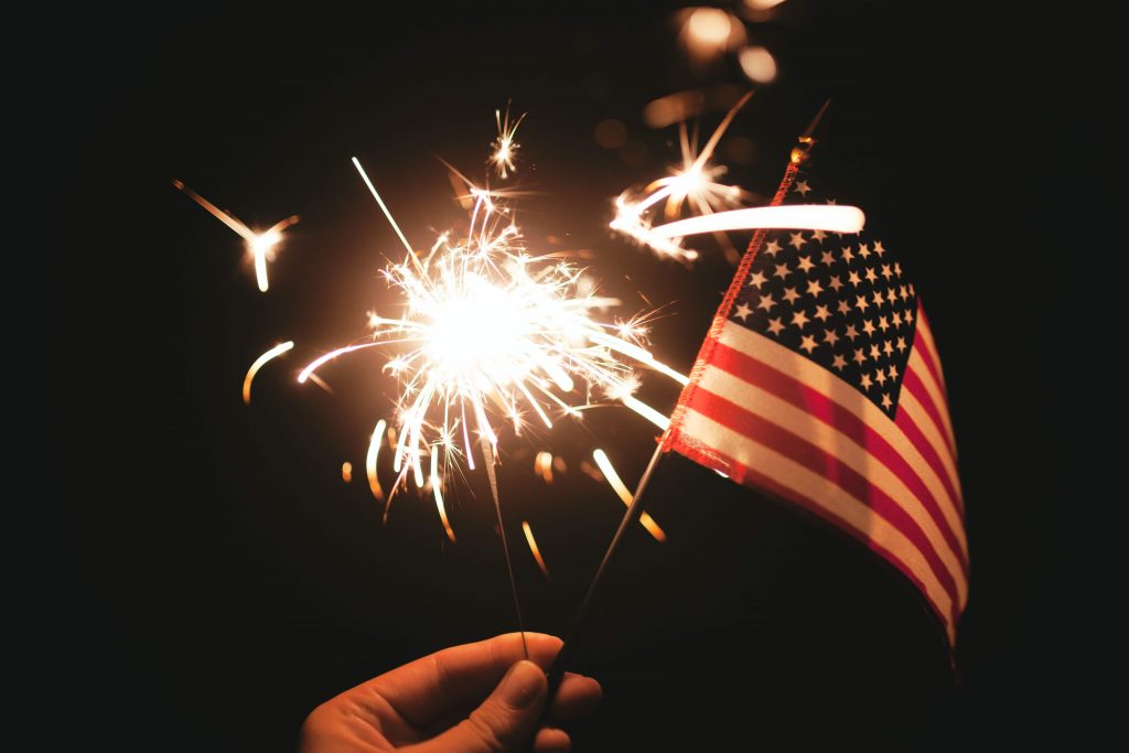 a hand holding a sparkler and US flag