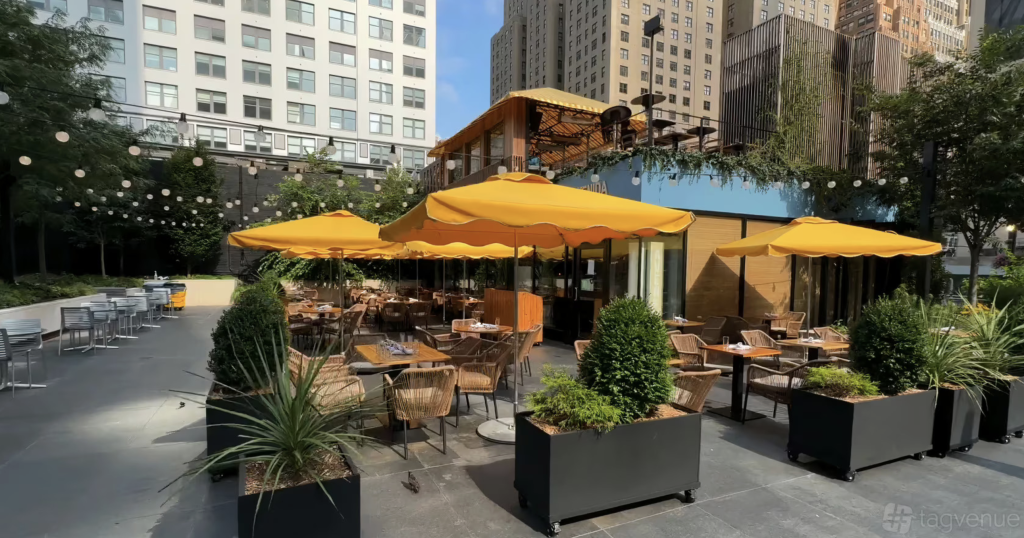 a lovely patio with potted plants and yellow parasols over square table and rattan chairs 