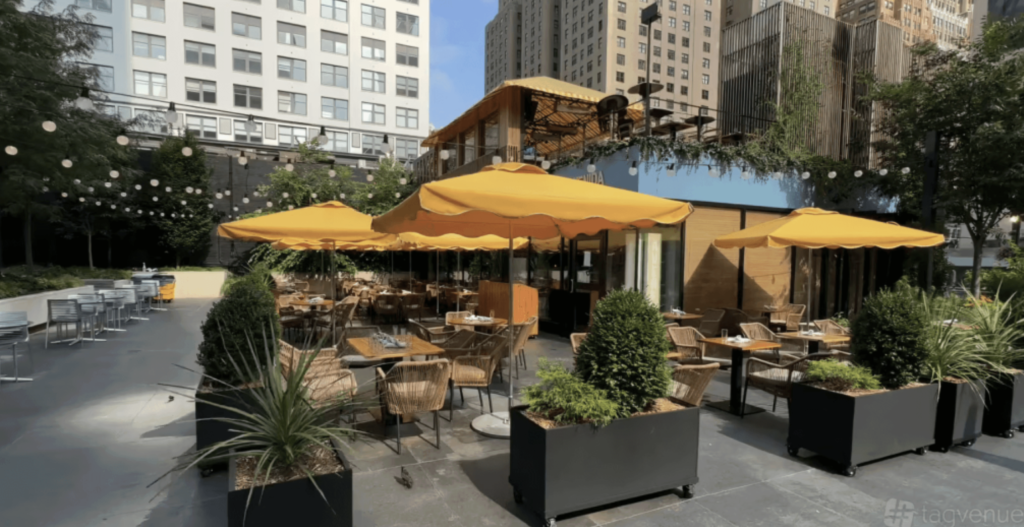 a lovely patio with potted plants and yellow parasols over square table and rattan chairs 