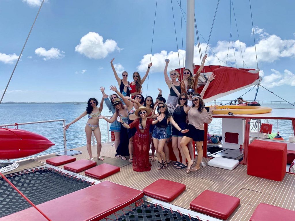 A group of smiling young people posing for a photo on a catamaran