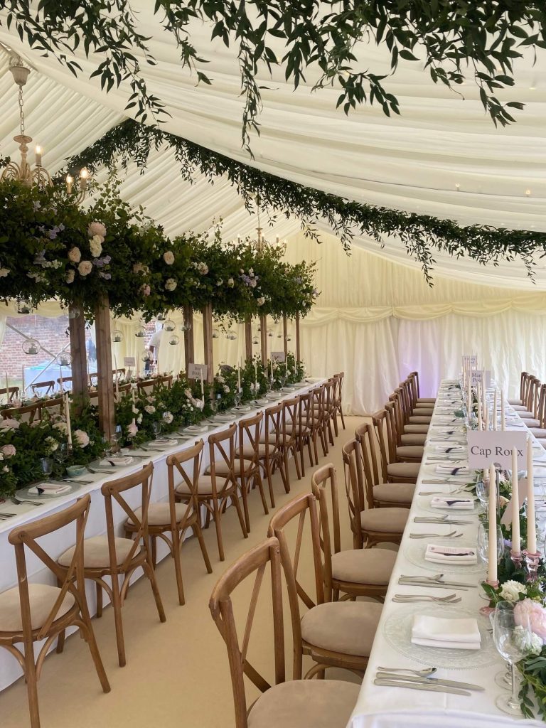A marquee wedding venue with two long tables decorated with white table cloths, flowers, and candles.