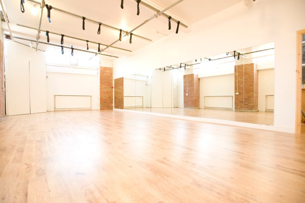 Spacious dance studio with natural wood flooring, large mirrors, and a ballet barre, bathed in natural light for an energetic birthday dance class.