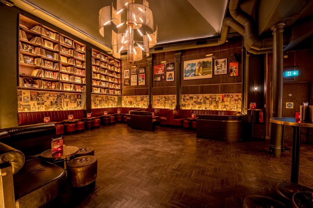 Backstage area of a live music bar with a library of vinyl records, plush seating, and mood lighting for a music-themed birthday celebration.