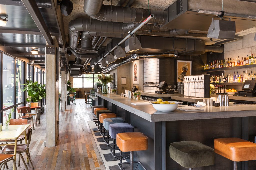 Stylish bar with an industrial-chic vibe, featuring exposed ductwork, mixed seating options, and a spacious bar area for a trendy birthday party.