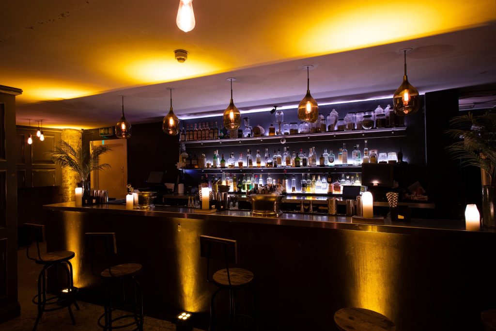 Chic cocktail bar with warm yellow lighting, a sleek black countertop, pendant lights, and minimalist bar stools for a modern birthday celebration.