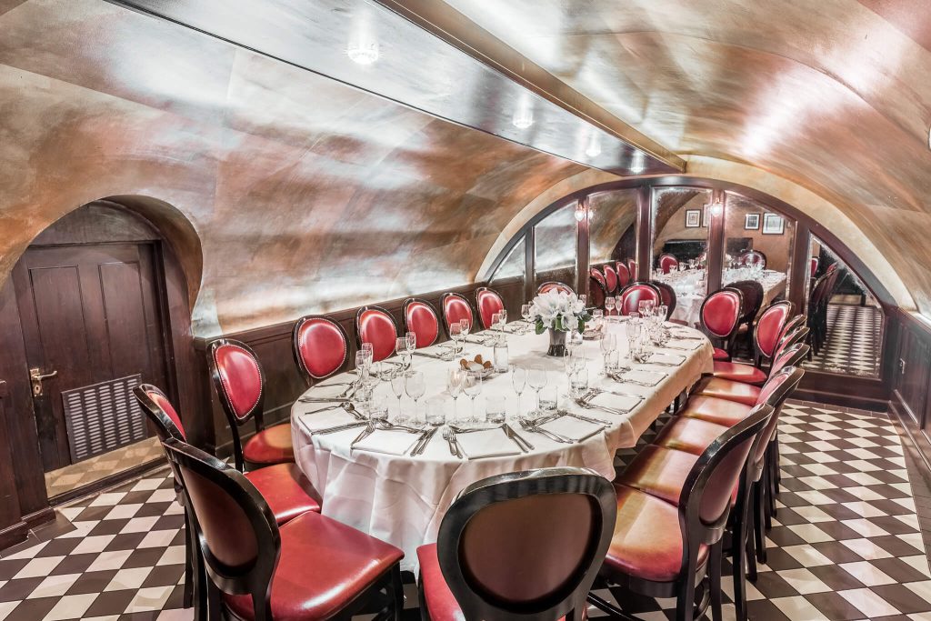 Elegant private vault dining space with red leather chairs, chequered floor, and a polished table setting under a curved metal ceiling for a unique birthday dinner.