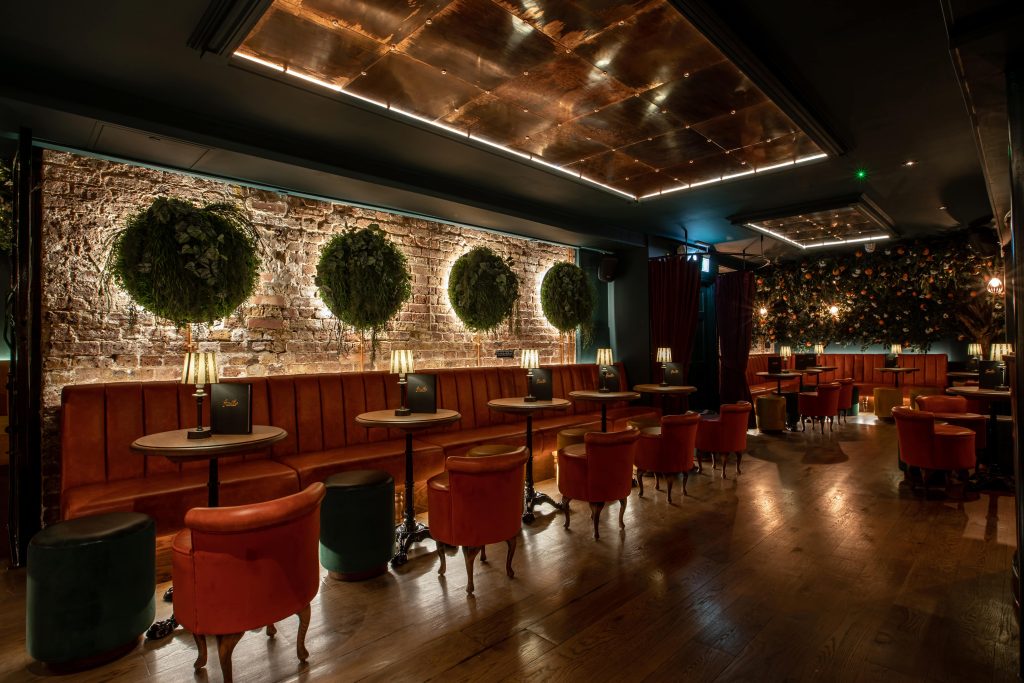 Sophisticated cocktail bar with leather banquettes, exposed brick walls adorned with topiary, and ambient lighting for a refined birthday celebration.