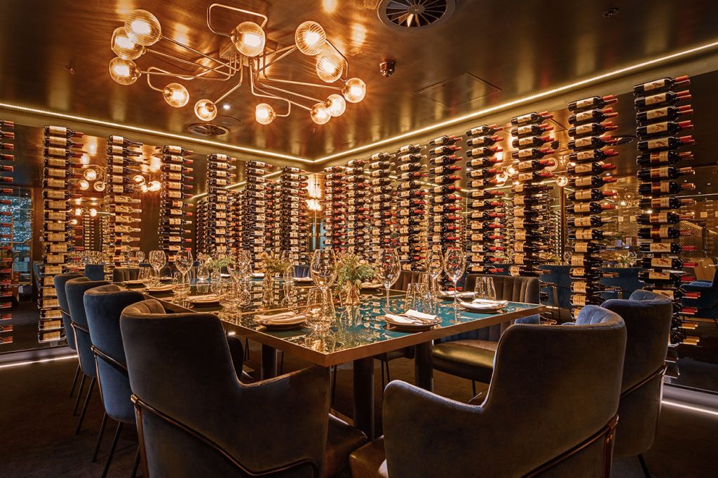 Chic wine room with a ceiling of glowing lights, surrounded by extensive wine racks and plush seating for an exclusive birthday dining experience.