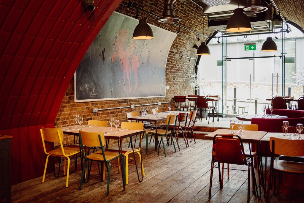 Rustic and stylish dining space with exposed brick walls, colourful chairs, and contemporary art, offering a welcoming atmosphere for a birthday meal.