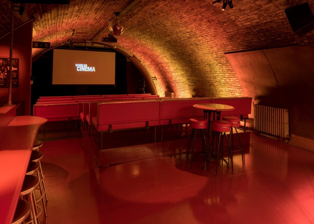 Underground cinema with exposed brick arches, red seating, and ambient lighting providing a unique cinematic experience for a birthday event.
