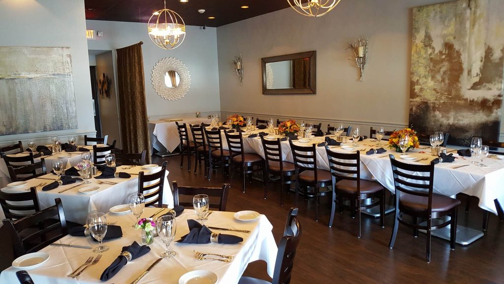 A modern and elegant dining room at Scotty's on Sheridan in Highwood, featuring white tablecloths with navy blue napkins, crystal glassware, and ambient lighting from geometric chandeliers. The walls are adorned with contemporary artwork and mirrors, contributing to the upscale and artistic atmosphere of the restaurant.