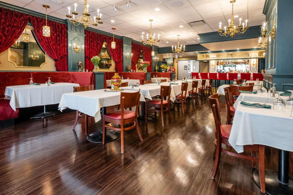 Elegant and sophisticated dining room at the Russian Tea Time Restaurant in Downtown Chicago, showcasing rich red velvet booths, white tablecloth-covered tables, and classic chandeliers. The restaurant features dark wood paneling and a well-stocked bar, with ornate decorative elements that evoke an old-world charm.