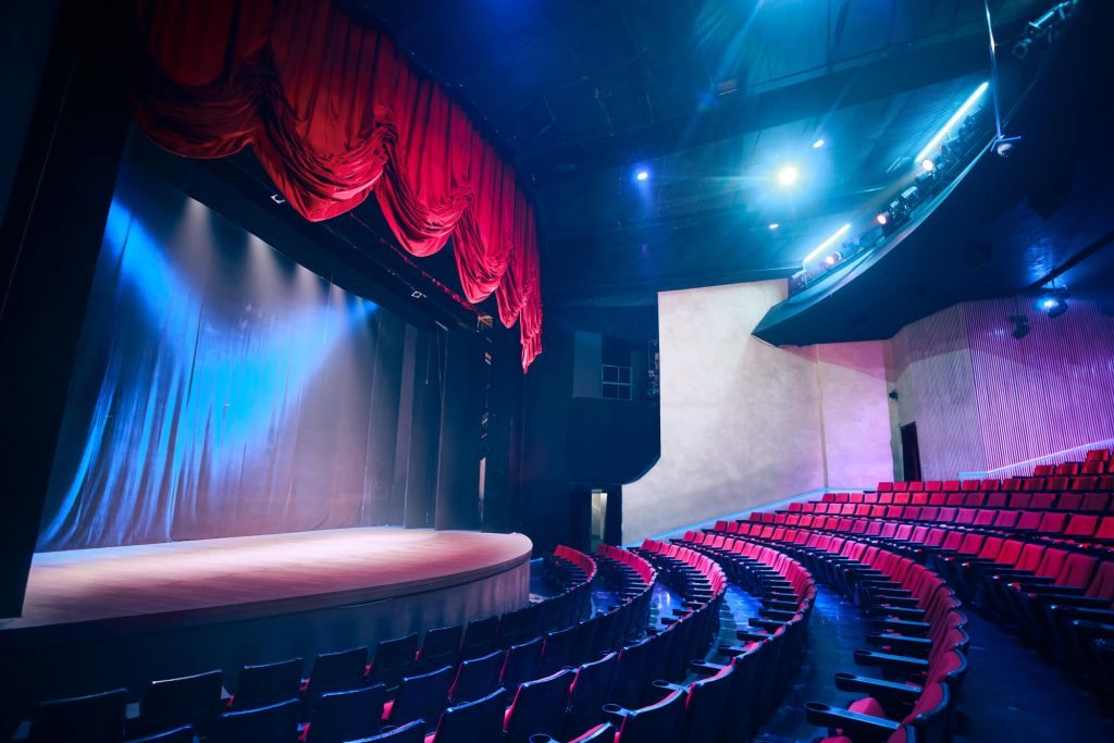 A theater with a spacious stage, red velvet curtains, and comfortable seating, ready for a Broadway show and a celebratory night out.