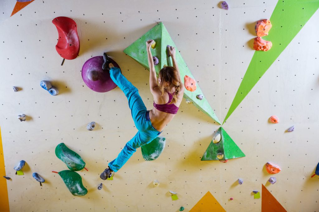 A climber scaling an indoor bouldering wall, with vibrant colored holds and geometric shapes, showcasing a challenging and engaging route.