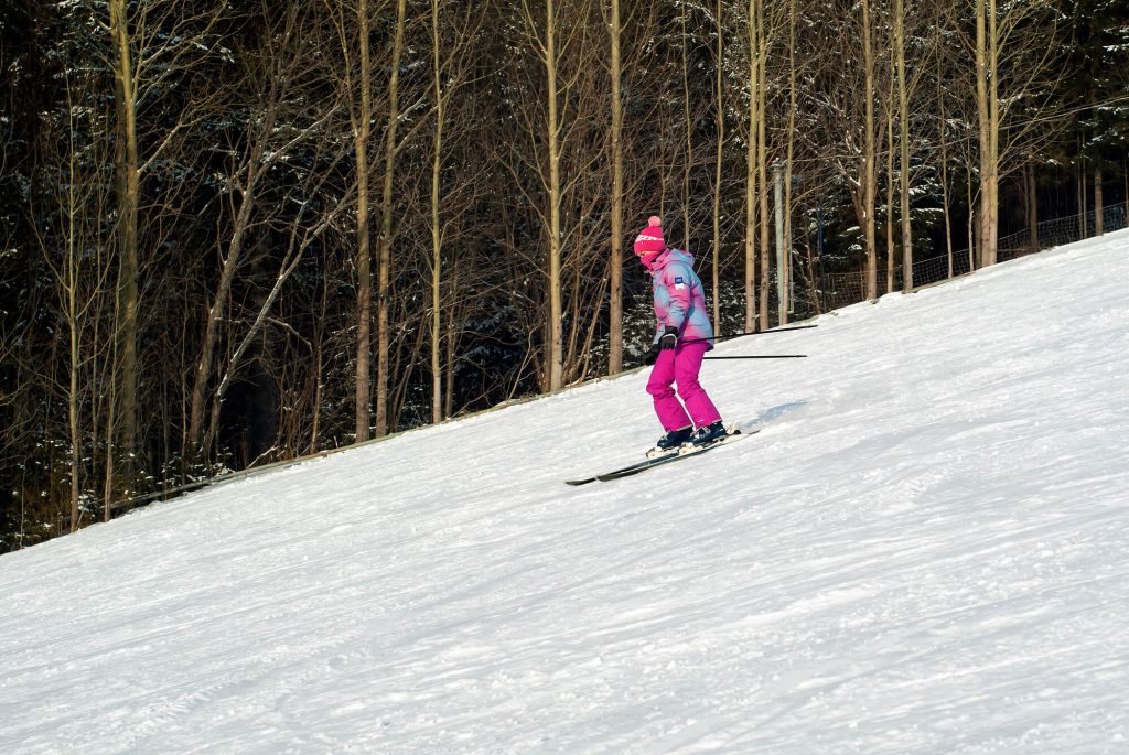 A skier in bright pink attire skiing down a snow-covered slope with a backdrop of leafless trees, demonstrating a leisurely descent on a clear day.