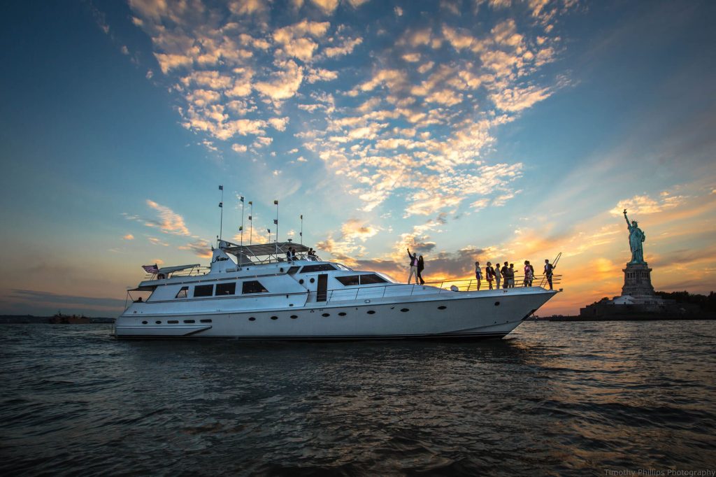 A yacht party at sunset with guests silhouetted against the skyline near the Statue of Liberty.