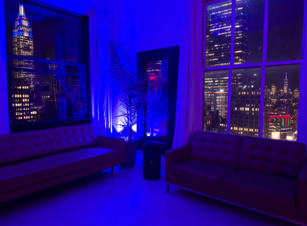 Lavish living room with plush sofas and striking blue lighting overlooking the Empire State Building at night in Manhattan.