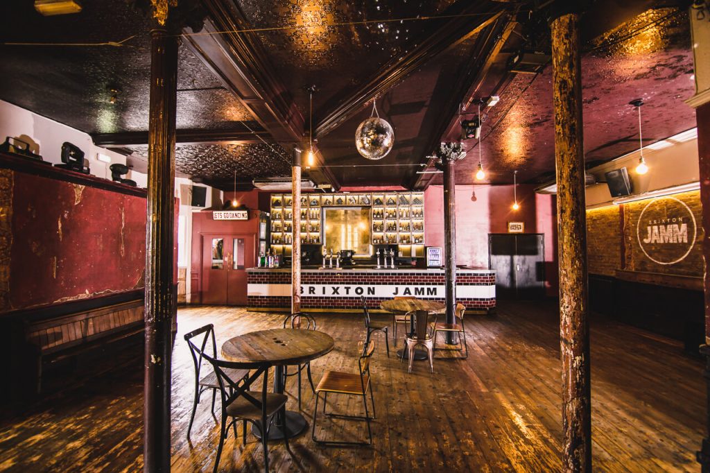 A vintage-style music venue with worn wooden floors, a disco ball, and a bar boasting a tiled façade, reflecting the eclectic spirit of Brixton.