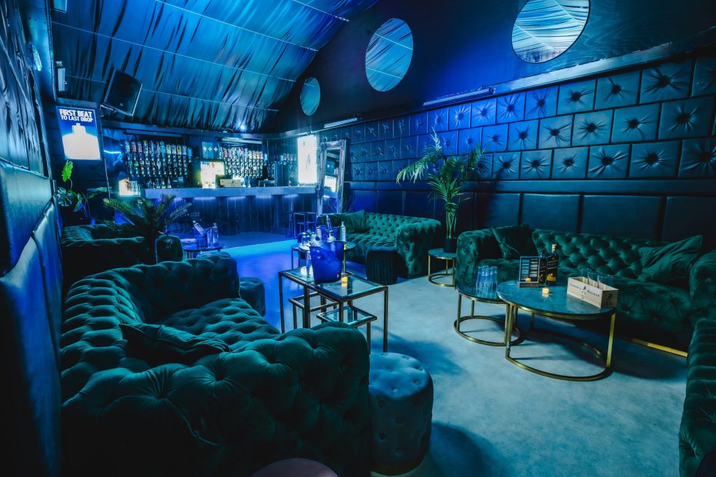 A futuristic blue lounge with plush velvet seating, geometric patterns, and ambient lighting, creating a luxurious and exclusive atmosphere.