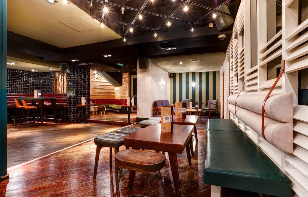 A spacious bar with eclectic seating, a mix of modern and rustic decor, and a striking black and white tiled floor, blending contemporary and classic styles.