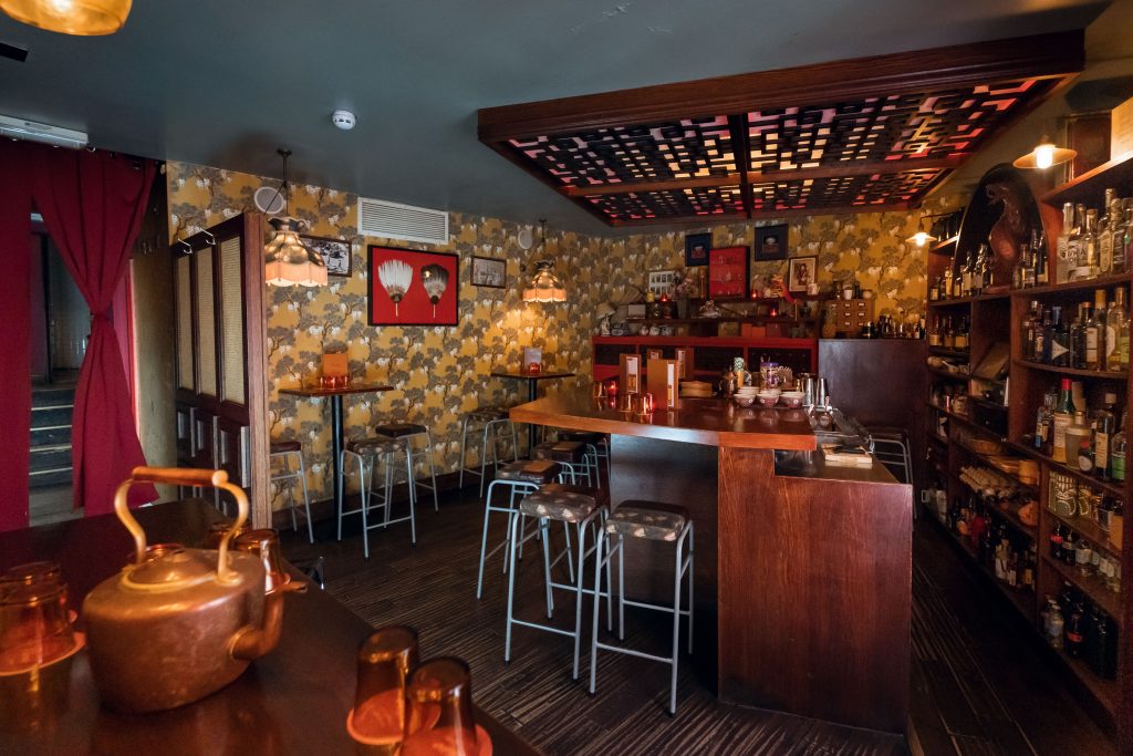 A cosy bar space with warm golden lighting, patterned wallpaper, and vintage Chinese-inspired decor, offering a unique drinking experience.