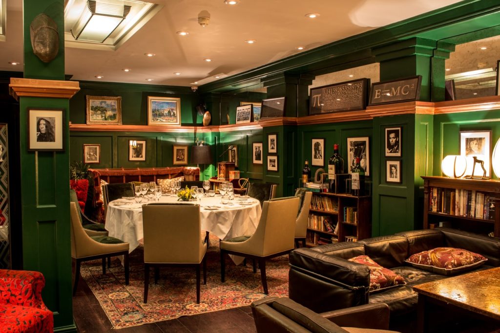 An elegant dining area with bookshelves, green panelled walls, and portraits, creating a sophisticated and cultured setting for meals.