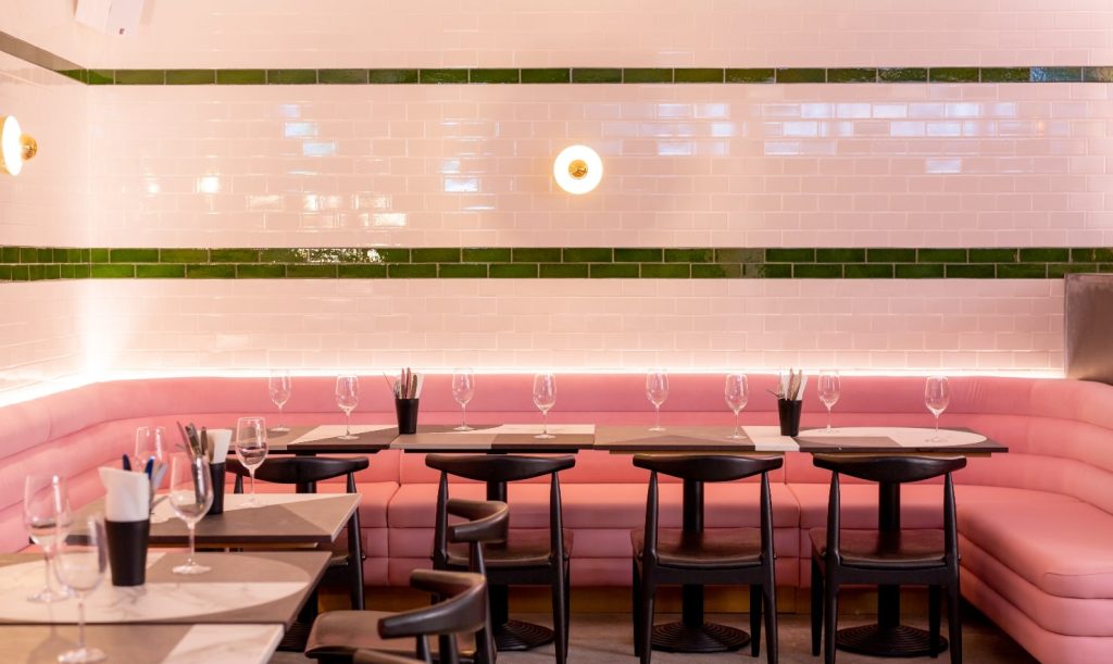 A contemporary dining space with a pink curved booth, white tiled walls, and chic simple decor, providing a modern and stylish vibe.