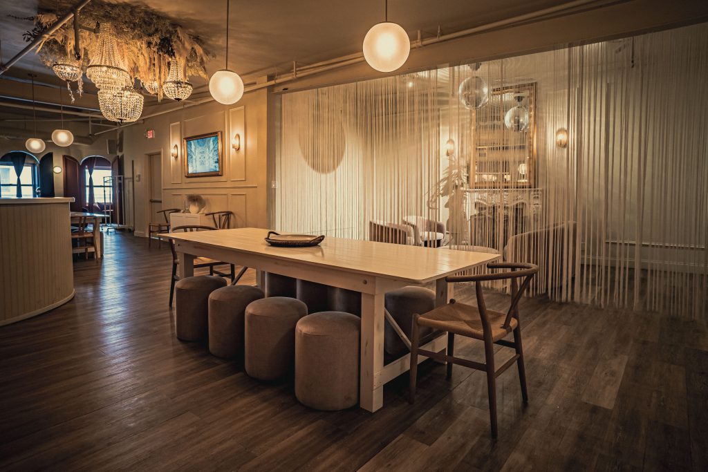 A modern and minimalist dining space in NYC for a dinner party with a long white table, plush seating, and spherical pendant lights.