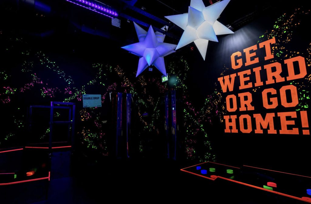 Neon sign with 'Get Weird or Go Home' message at a vibrant London venue for quirky birthday ideas for him.