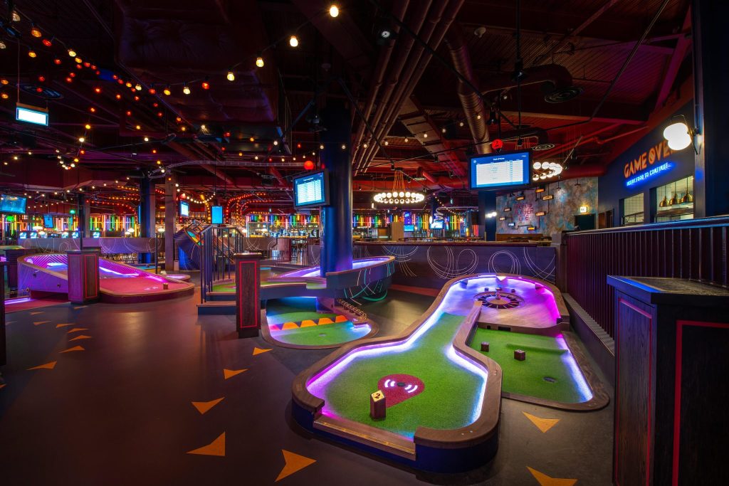 Futuristic indoor mini-golf course at Puttshack in White City, London, with glowing play areas and a lively bar, perfect for an entertaining stag do event