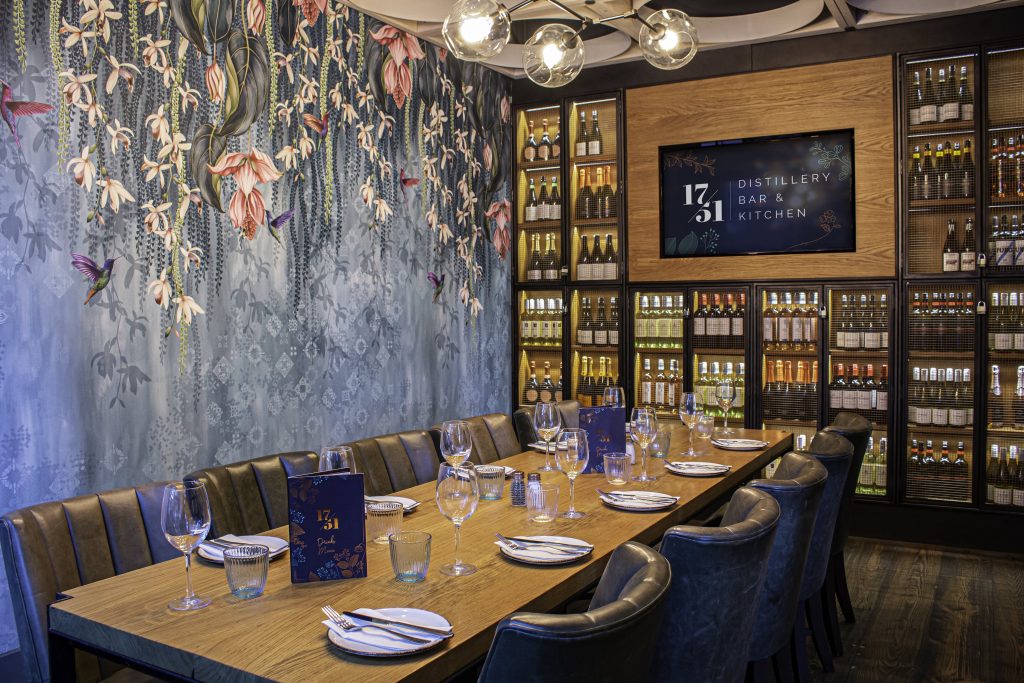 Elegant dining setup at 1751 Gin Distillery, London, with floral wallpaper and wood-paneled bar for a sophisticated stag do