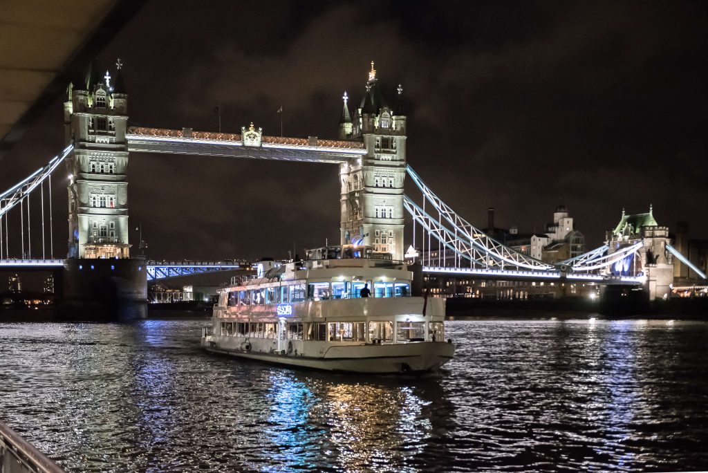 Night view of a private party cruise boat sailing on the Thames River with Tower Bridge in the background for a stag party in London