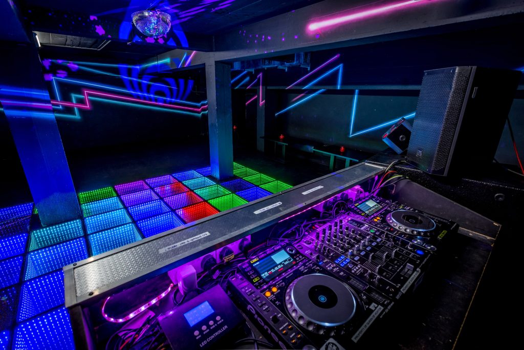 Neon-lit DJ booth and dance floor at Queen of Hoxton discotheque in Shoreditch, London, ready for a stag party