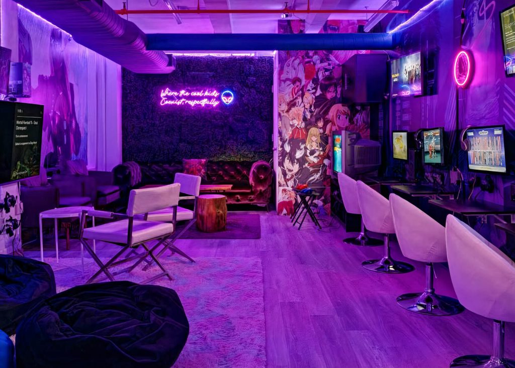 A neon-lit game room with anime wall art, plush seating, and gaming consoles.